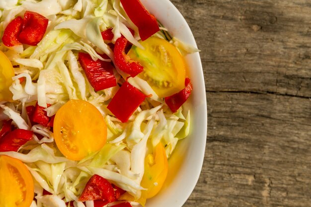 Fresh vegetable salad with cabbage, yellow tomatoes and red sweet pepper on rustic wooden table. Top view