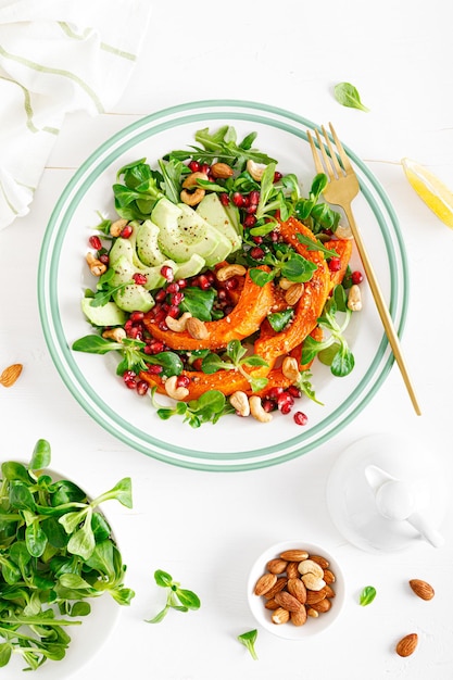 Fresh vegetable salad with lambs lettuce baked butternut squash or pumpkin avocado pomegranate cashew and almond nuts Healthy vegetarian food concept Top view