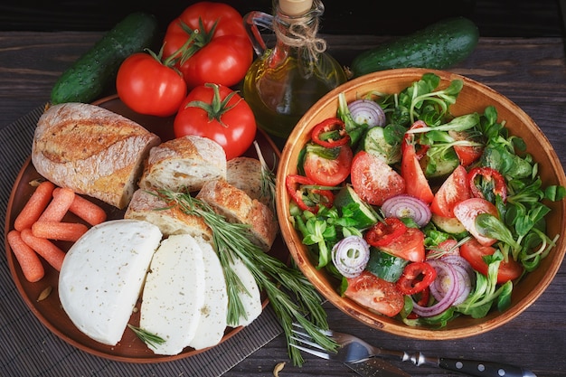 Insalata di verdure fresche con pomodori, cetrioli e cipolle. servito con formaggio, verdure, olio d'oliva e pane