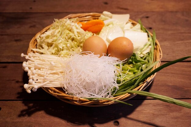 Fresh Vegetable Set Morning Glory Chinese Cabbage Carrot Sliced Cabbage and golden needle mushroom with 2 fresh eggs and Bean vermicelli Place in a basket on a wooden table