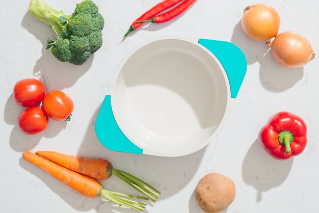 Fresh vegetables around white pot