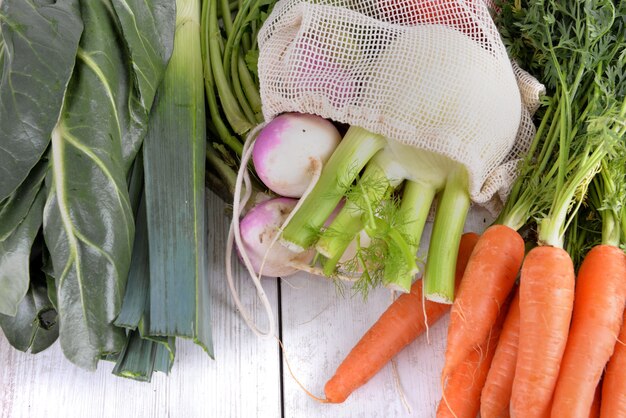 Fresh vegetables in a bag among other fresh vegetables on a white table