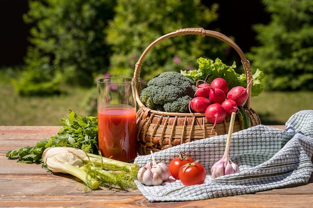 Fresh vegetables in a basket and tomato juice over green nature.