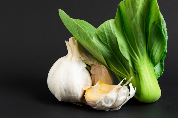 Фото Свежие овощи: бок чой или китайская капуста и чеснок на черном фоне. здоровая пища.