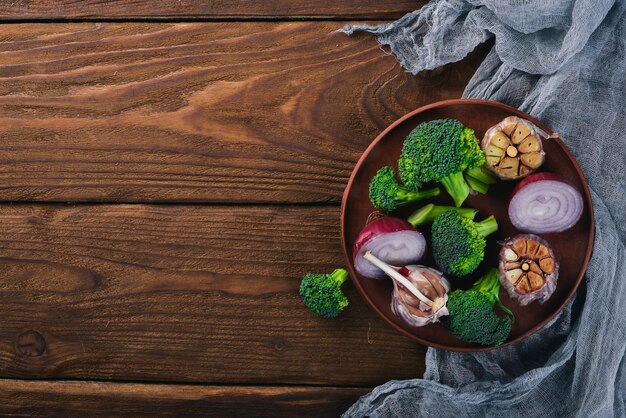 Fresh vegetables on a clay plate On a wooden background Top view Free space for your text