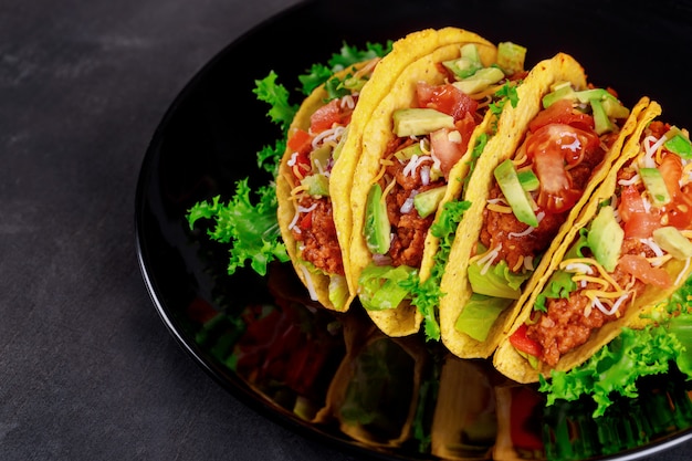 나무 배경에 검은 접시에 맛있는 타코에 신선한 야채