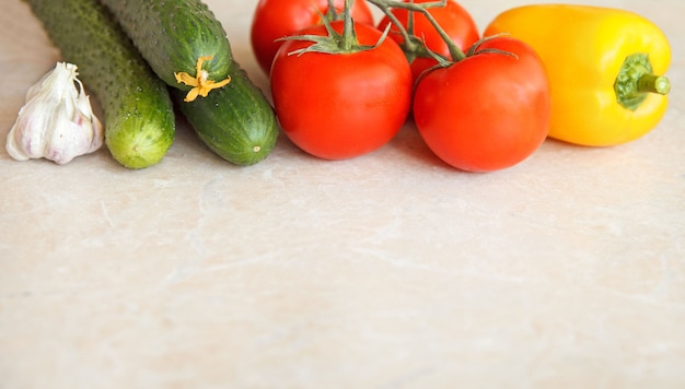 Свежие овощи разного цвета, огурцы, помидоры, сладкий перец, чеснок на светлом фоне