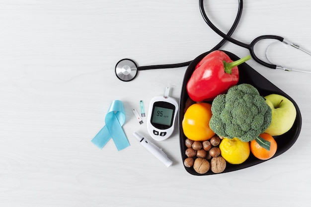 Fresh vegetables and fruit with glucometer top view on white wooden background