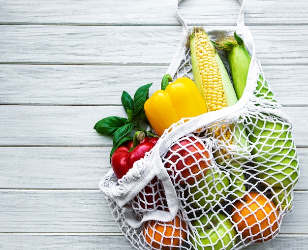 Fresh vegetables and fruits on eco string bag on a white wooden.