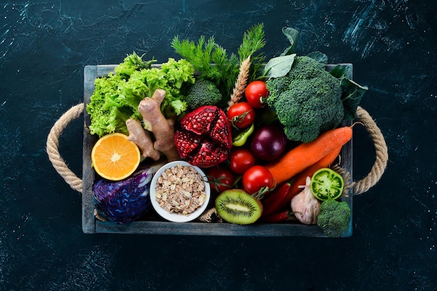 Fresh vegetables and fruits in a wooden box on a black background. Organic food. Top view. Free copy space.