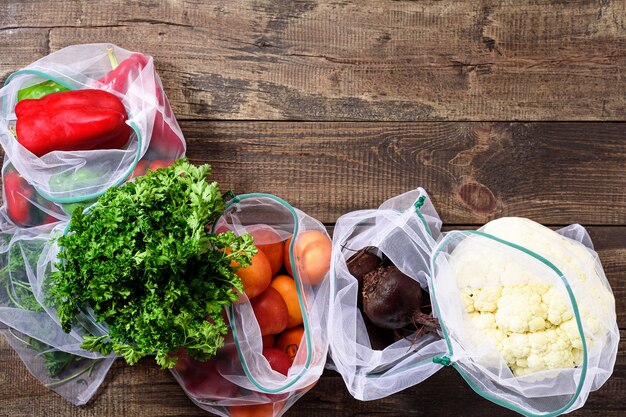 Fresh vegetables and greens in reusable eco-friendly pouches on wooden brown background with copy space