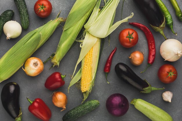 Fresh vegetables on grey background Corn zucchini eggplant red chilli and bell pepper cucumber and onion on rustic table top view Organic cooking ingredients