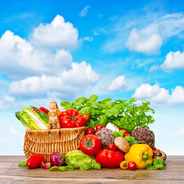 Fresh vegetables and herbs on wooden background over beautiful blue sky. Shopping basket with organic food ingredients