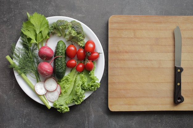 灰色のテーブルの上の白い皿に新鮮な野菜