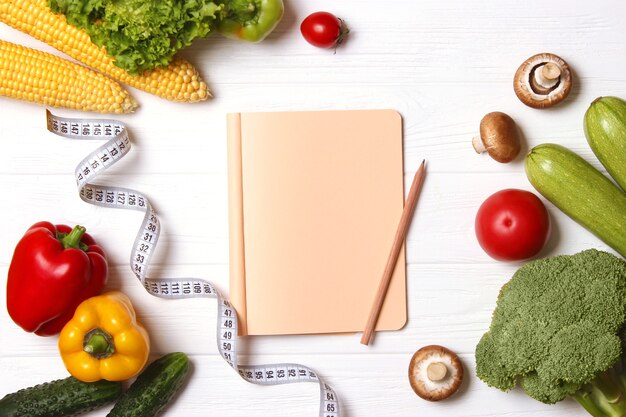 Fresh vegetables measuring tape and paper notepad on wooden table