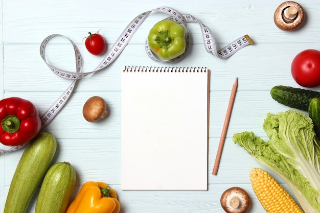 Fresh vegetables measuring tape and paper notepad on wooden table