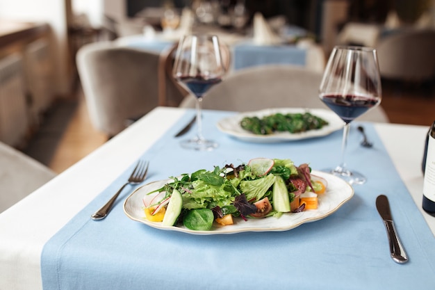 Fresh vegetables salad on the served restaurant table with glasses of red wine