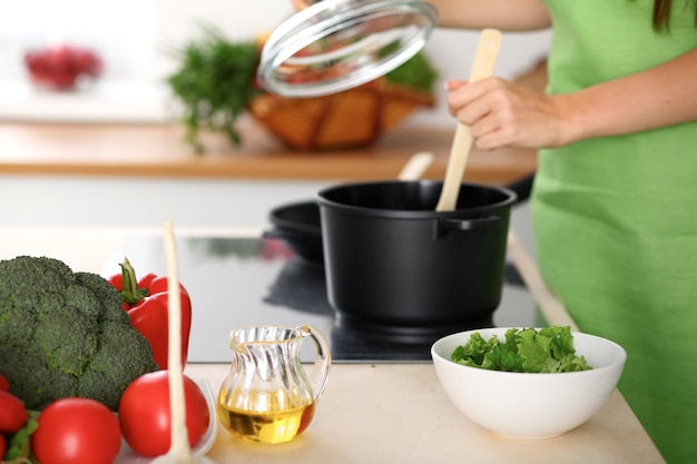 Foto verdure fresche, insalata e olio vegetale sullo sfondo della donna sta cucinando ai fornelli in cucina