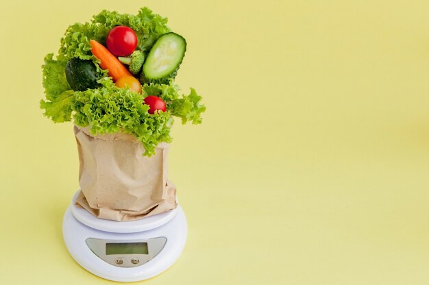 Fresh vegetables on scales on yellow background. Vegan and healthy concept.