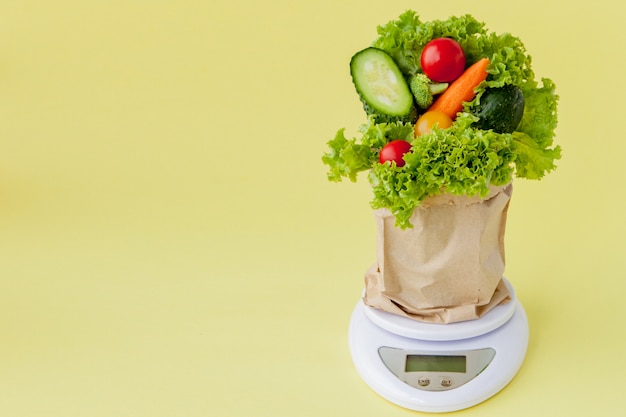 Fresh vegetables on scales on yellow background. Vegan and healthy concept.