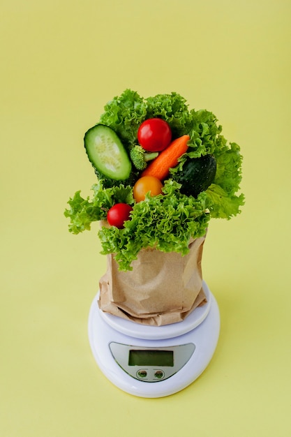 Fresh vegetables on scales on yellow background