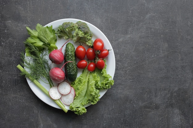 Verdure fresche in un piatto bianco su un tavolo grigio