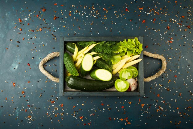 FRESH VEGETABLES ON WOODEN BOX ON A DARK STONE. THE CONCEPT OF VINTAGE. THE YOUNG CORN ONIONS ASPARAGUS GREEN TOMATO CUCUMBER ON A DARK SURFACE.