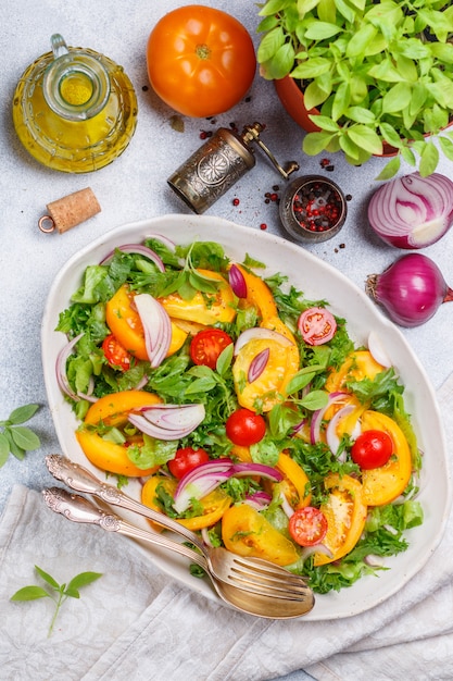 Fresh vegetarian salad of colorful tomatoes, red onions, lettuce and basil with spices and olive oil in a white plate