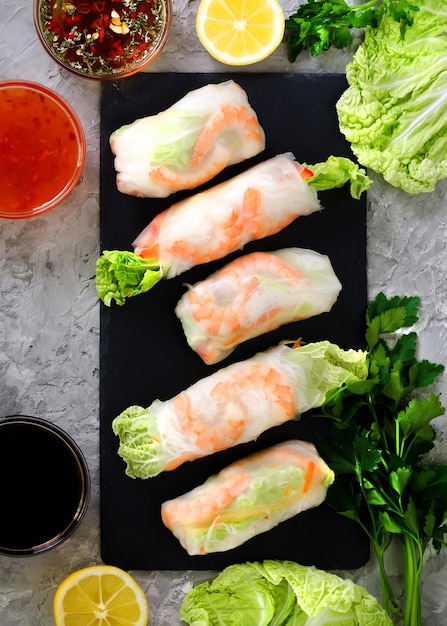 Photo fresh vietnamese asian chinese food frame on grey concrete background spring rolls rice paper lettuce salad vermicelli noodles shrimps fish sauce sweet chili soy lemon top view