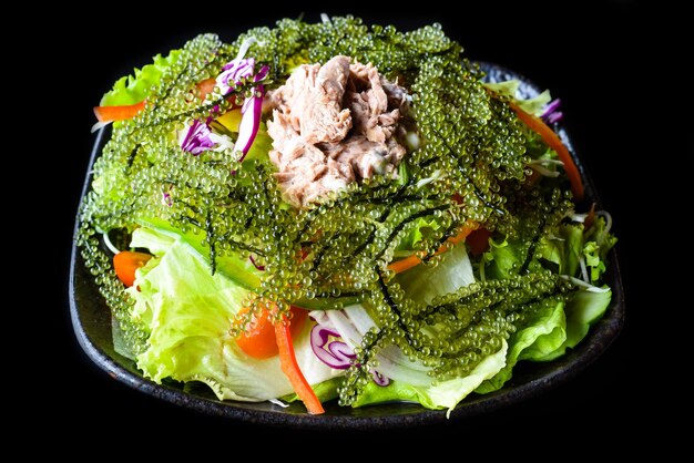 Fresh Vietnamese salad with vegetables, tuna and sea grape on black background side view