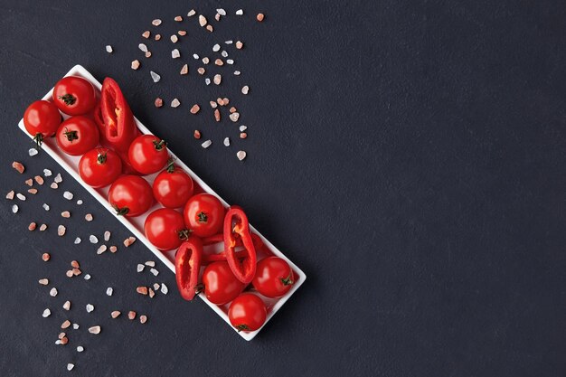 Fresh washed cherry tomatoes and paprika slices on a white oblong dish with pink salt on a black concrete table