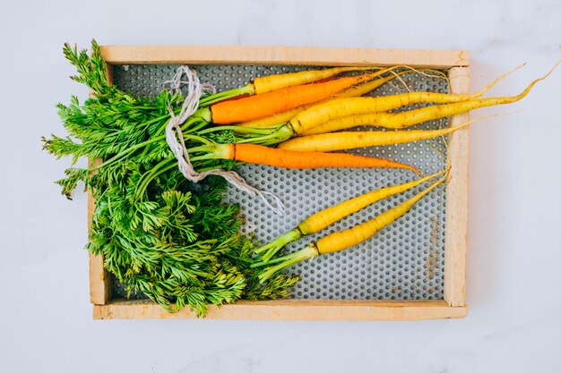 Fresh washed yellow and orange carrots on wooden tray on a marble