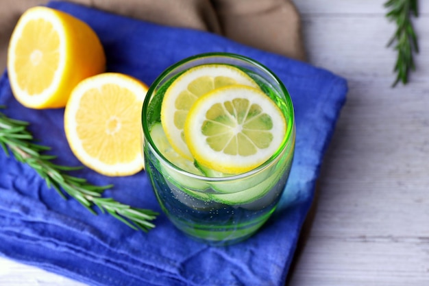 Fresh water with lemon and cucumber in glassware on napkin on wooden table closeup