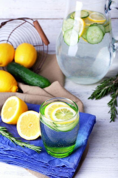 Fresh water with lemon and cucumber in glassware on napkin on wooden table closeup