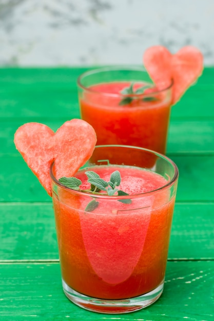 Fresh watermelon blended drink with mint leaves and a heart of watermelon in glasses on a wooden table. 