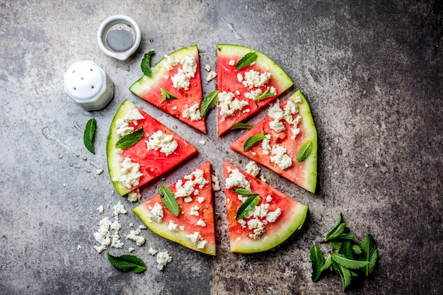 Fresh watermelon pizza salad with feta cheese, mint, salt and oil on stone