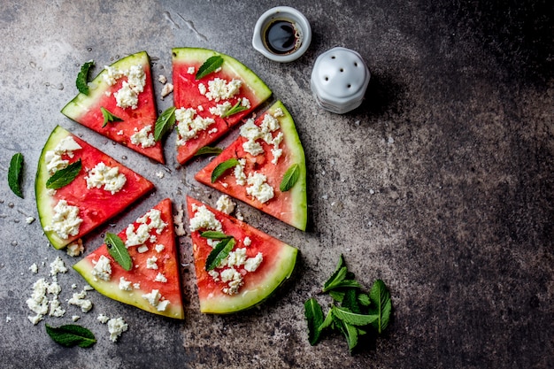 Fresh watermelon pizza salad with feta cheese, mint, salt and oil on stone