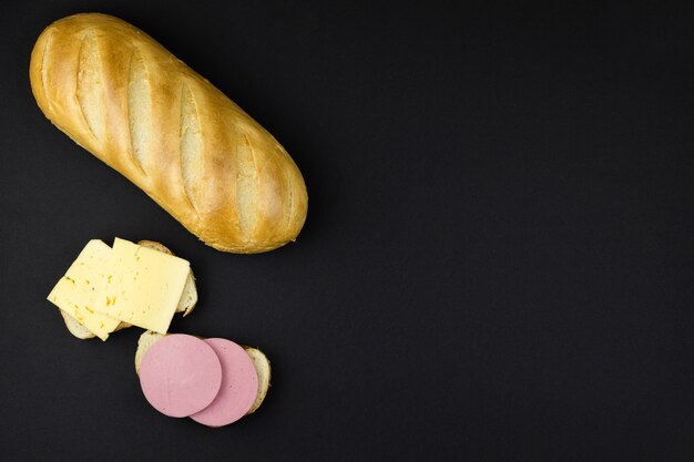 Fresh wheat loaf of white bread and sandwiches with cheese and sausage on a black background