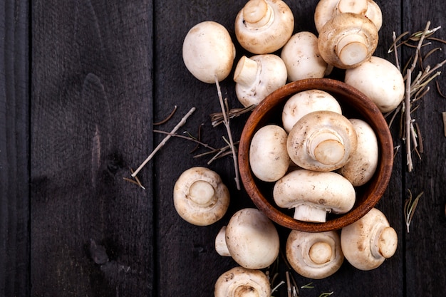 Fresh white mushrooms champignon in bowl on dark wooden background. 