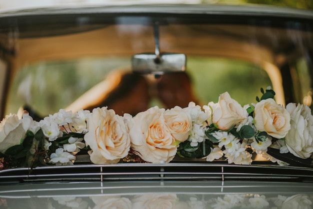 Свежие белые розы на заднем стекле свадебного автомобиля