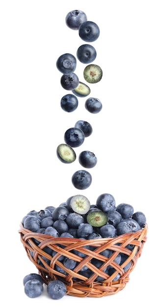 Fresh whole blueberries falling into wicker basket on white background