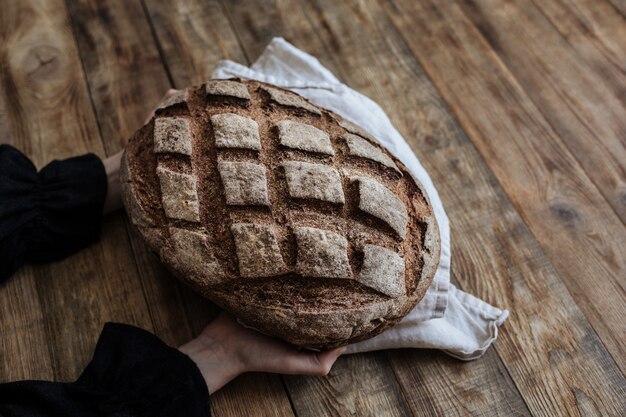 Fresh whole grain bread on a wooden table in the hands of a child