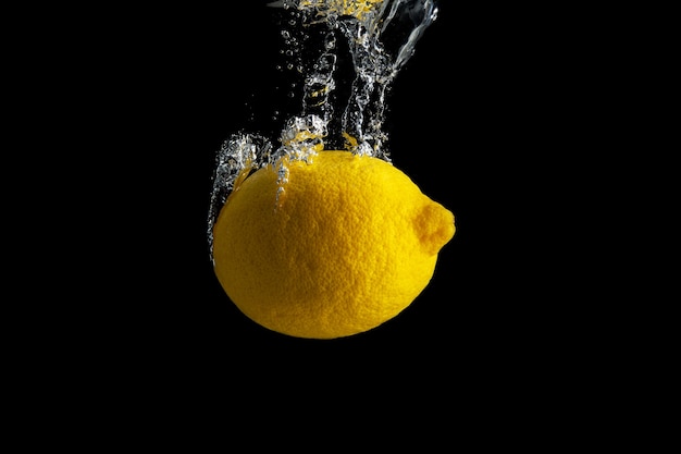 Limone giallo fresco nella spruzzata dell'acqua isolata sul nero.