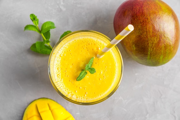 Fresh yellow mango smoothie in a glass with straw fresh fruits and mint Summer tropical drink