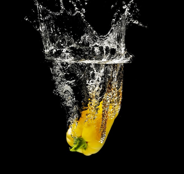 Fresh yellow pepper falling in water on dark background