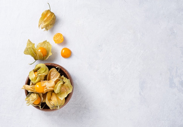 Fresh yellow physalis in wooden bowl on white background. top view and copy space