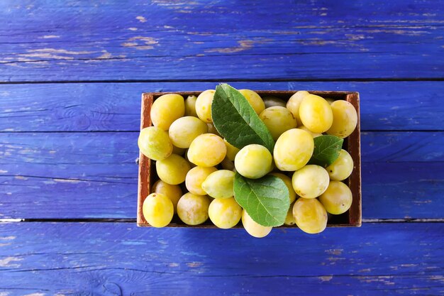 Foto prugne gialle fresche frutti maturi in una scatola di legno su sfondo blu