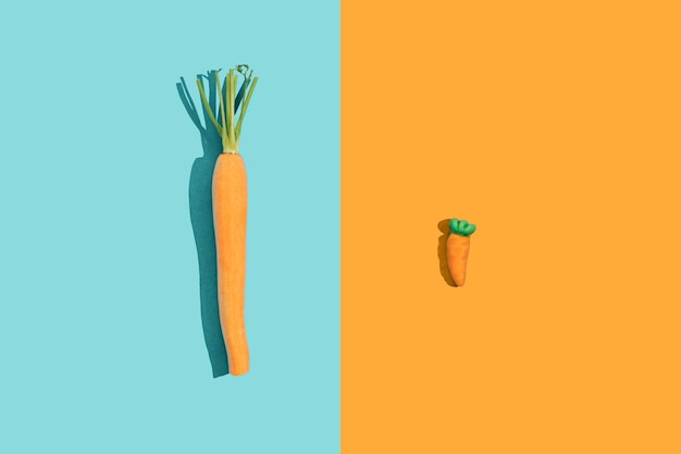 Fresh young bio orange carrot with green leaf haulm and a candy gummy carrot on a bright blue background with copy space with sharp shadows Healthy diet eating vs junk food concept Raw food idea