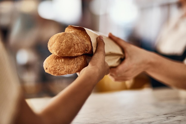 Freshly baked bread one of lifes simplest pleasures Cropped shot of a woman buying freshly made baguettes at a bakery