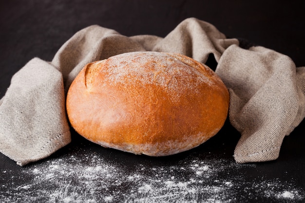 Freshly baked  bread with flour and kitchen towel on black background